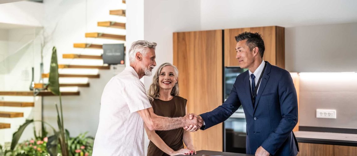 Senior couple signing house leasing agreement and shaking hands with asian real estate agent